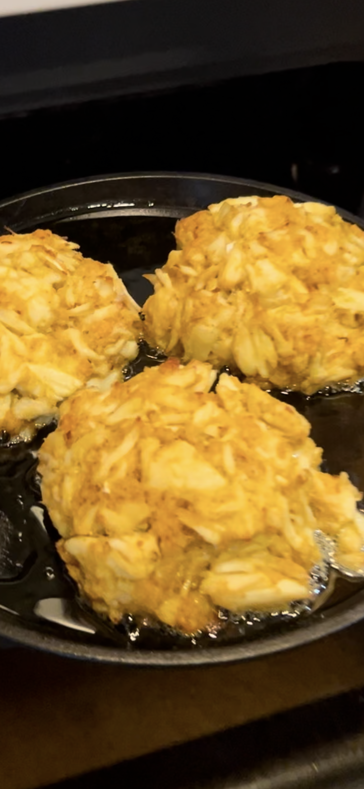 3 jumbo lump Blue Crab crab cakes made with Blue Ember Spice Rub, on an iron skillet, being sautéed to a golden brown 