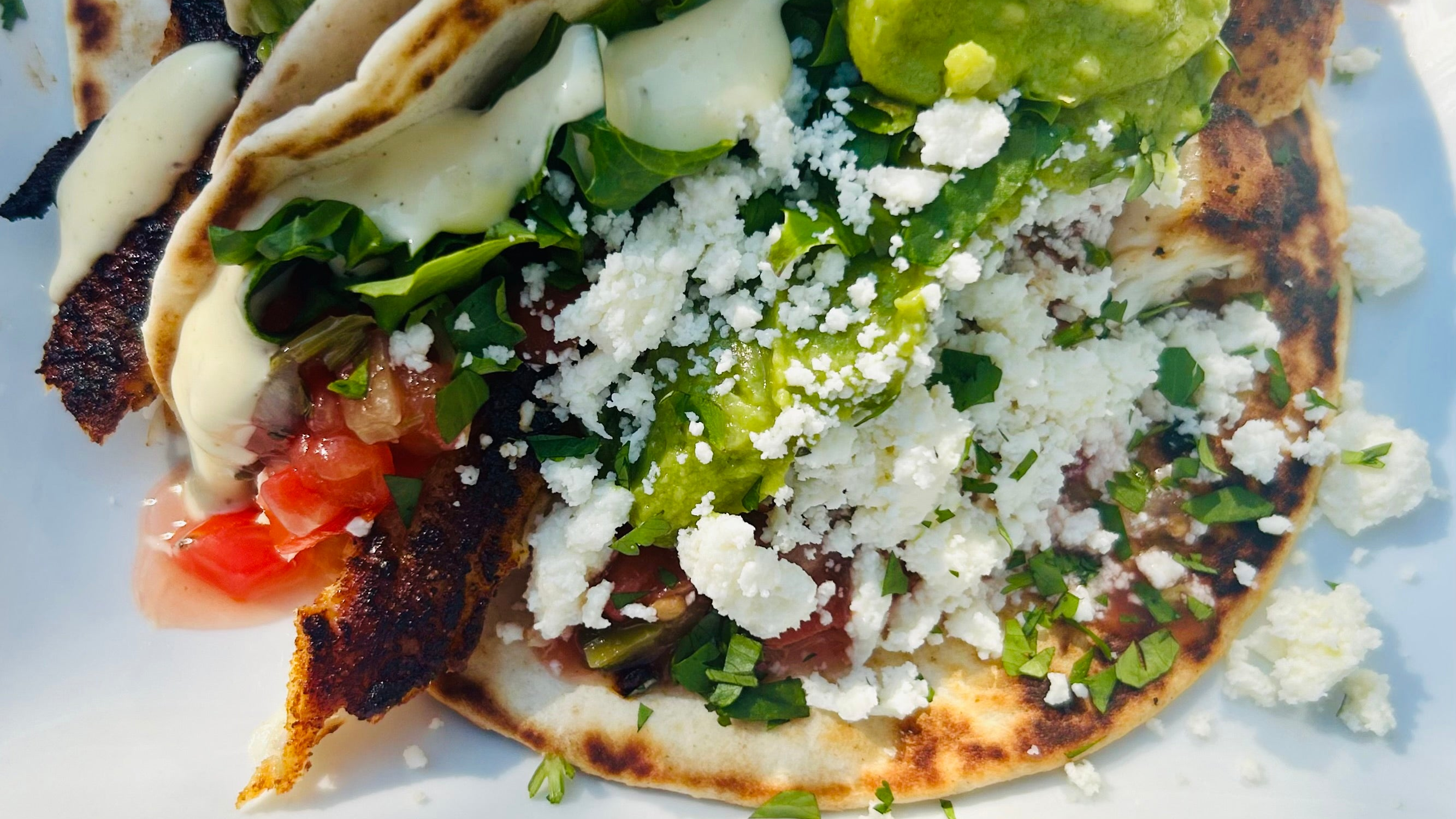 grilled red snapper seasoned with Blue Ember Spice Rub in a soft taco shell with lettuce, tomato, guacamole, feta cheese, and avocado aioli