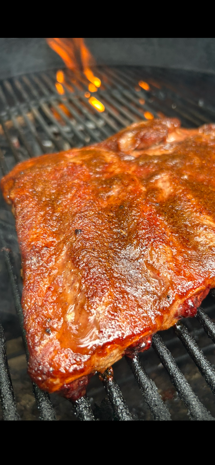 Blue Ember seasoned ribs on a charcoal Weber grill with flame showing