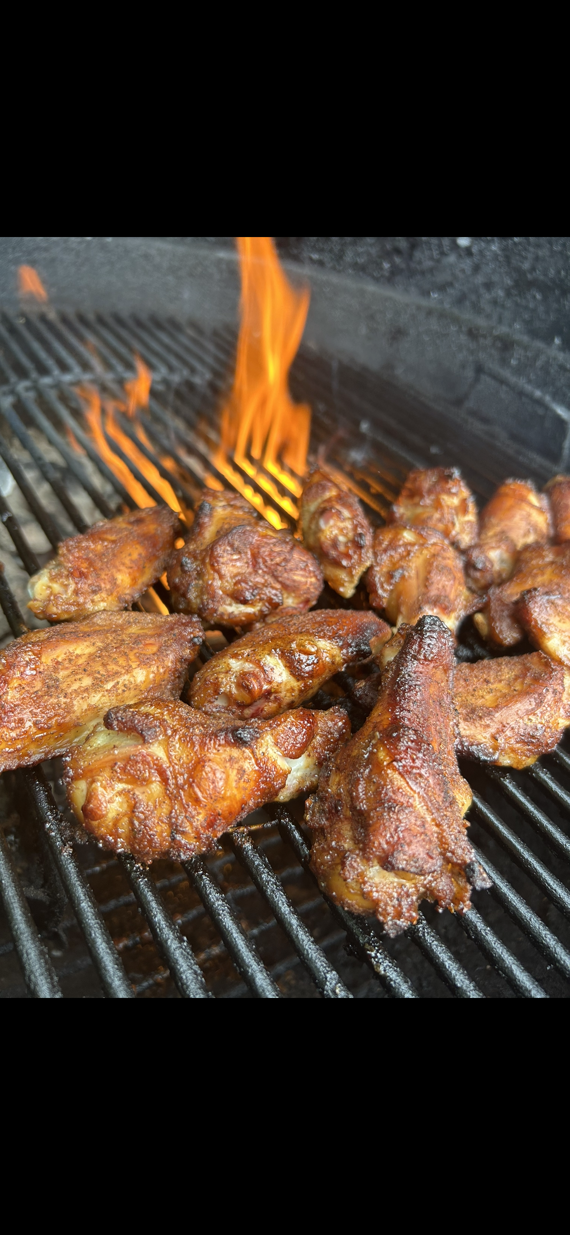 halved chicken wings on a charcoal Weber grill, seasoned with Blue Ember Spice Rub, with flame showing