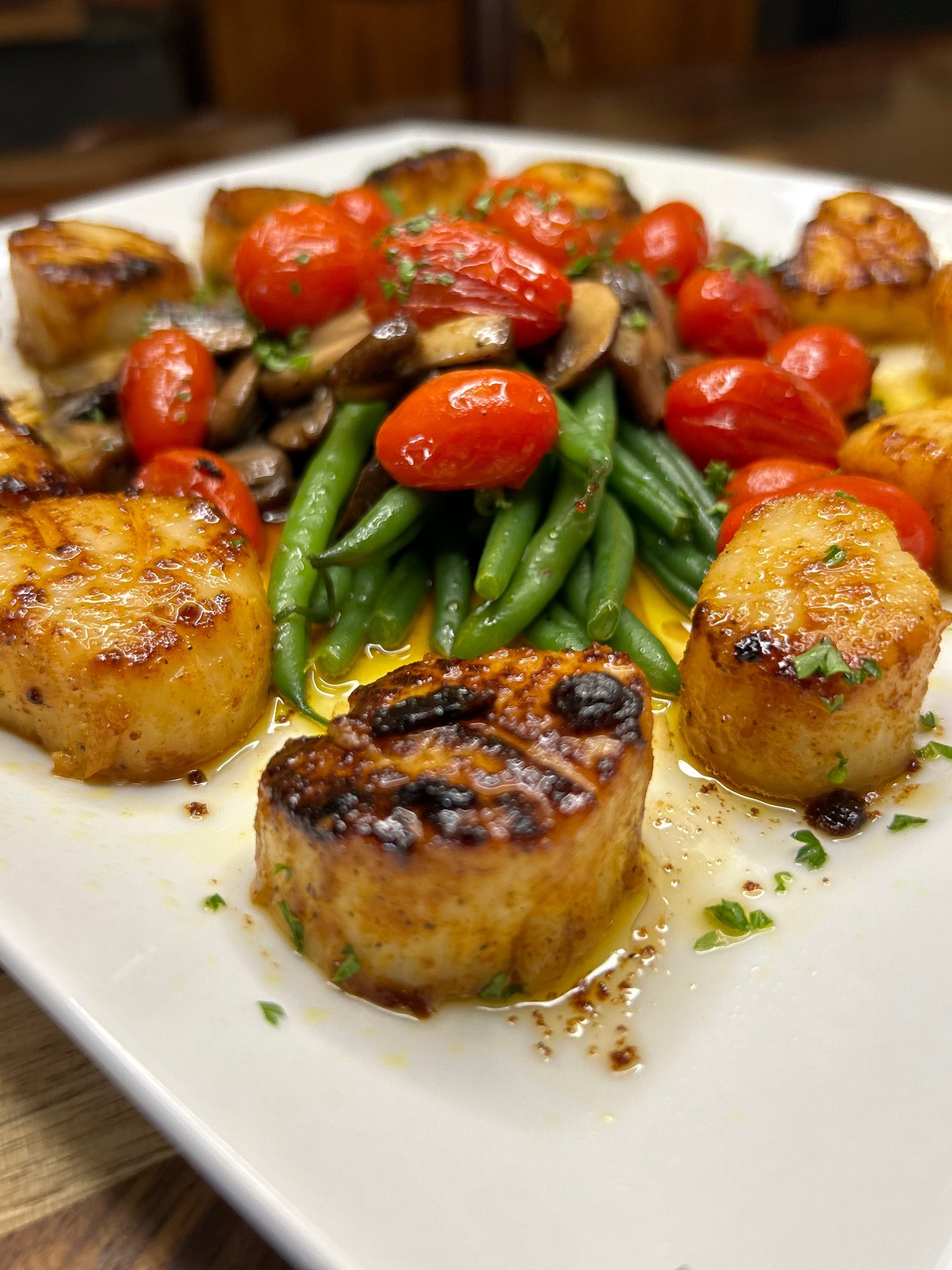 Sautéed sea scallops seasoned with Blue Ember Spice Rub, circling fresh green beans, sautéed cherry tomatoes, and buttered slivered mushrooms